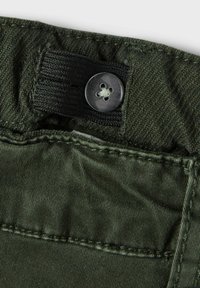 Fascia in tessuto verde scuro con un elastico nero e un bottone nero. Presenta cuciture visibili e una texture liscia.