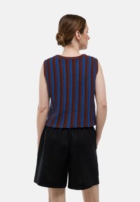 Haut sans manches en tricot avec des rayures verticales brunes et bleues, tissu texturé, encolure ronde, associé à un short noir. Vue de dos.