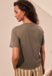 T-shirt verde oliva a maniche corte con vestibilità comoda, caratterizzata da un design semplice e una texture morbida. La cucitura dettagliata corre lungo la schiena.