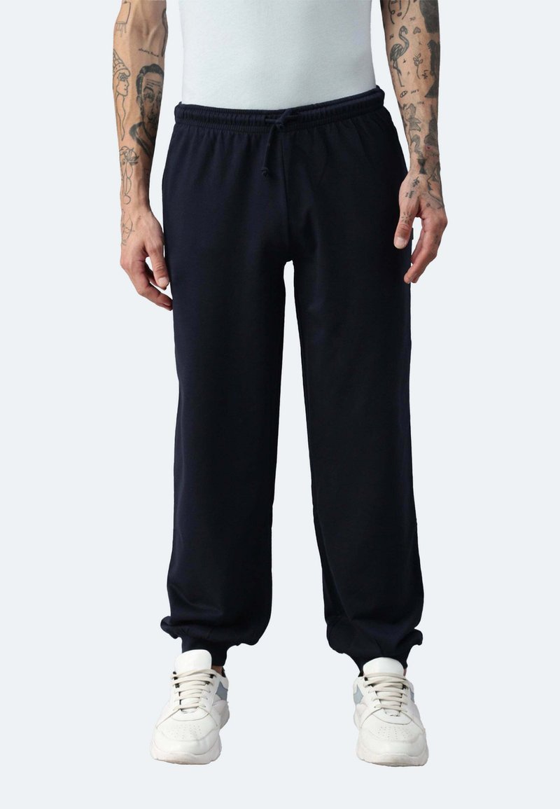 Navy Jogginghosen mit elastischem Bund und Bündchen, aus weichem Material. Kombiniert mit weißen Sneakers, von der Hüfte abwärts präsentiert.