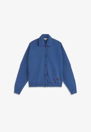 Veste bleue boutonnée avec col, manches longues, poignets côtelés et une petite pièce noire près de l'ourlet sur le côté droit avant.