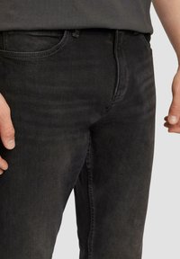 Jeans en denim noir avec une coupe slim, dotés d'une taille mi-haute, de poches avant et d'un effet d'usure subtil sur les cuisses.