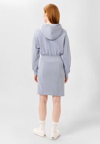 Felpa azzurra chiara con cappuccio regolabile, cintura a coste e gonna abbinata. Texture liscia; presenta maniche lunghe e cuciture minime.