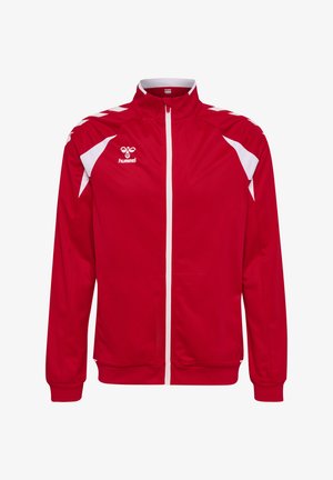 Rote Sportjacke mit weißem Reißverschluss, weißen Chevron-Streifen auf den Schultern, weißen Seitenteilen und einem hummel-Logo auf der linken Brust.