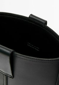 Black leather bag with smooth texture, round shape, and minimalistic design. Features a top handle and open interior. Stitched accents visible.