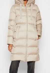 Abrigo acolchado beige con capucha, con cremallera completa, mangas largas y diseño acolchado. Hecho de tela suave y ligera.