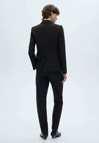 Dark brown suit featuring a fitted jacket with a single vent, matching trousers, and black shoes. Smooth texture, classic design.