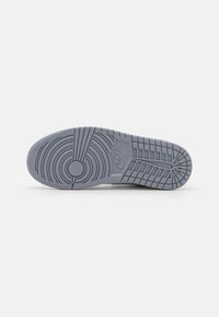 Semelle en caoutchouc grise d’une chaussure Nike montrant des motifs de bande de roulement circulaires et rectangulaires avec le logo Nike au centre.