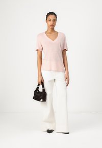 T-shirt rosa chiaro con scollo a V realizzata in tessuto morbido, abbinata a pantaloni bianchi a gamba larga. Borsa nera strutturata con manico corto.