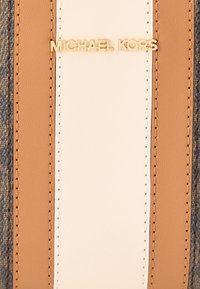 Πατς Michael Kors με χρυσά γράμματα, που διαθέτει υλικά σε μπεζ, εκρού και σκούρο γκρι με υφή, δείχνοντας καθαρό, γραμμικό σχέδιο και ραφές.