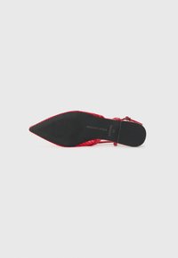Chaussure à bout pointu rouge avec une tige texturée et une semelle en caoutchouc noir. Bride de cheville avec détail de boucle pour un maintien sécurisé. Silhouette élégante et élancée.