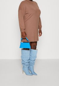 Braunes oversized Pulloverkleid mit langen Ärmeln, kombiniert mit hellblauen, lässigen kniehohen Stiefeln und einer kleinen blauen Handtasche.