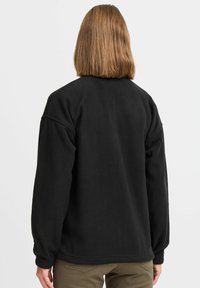 Must musta pullover, millel on lõdva lõige, madalad õmblused ja elastsed mansetid, mis on valmistatud siledast materjalist ning millel on minimaalne kaunistus.