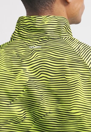 Man wearing a high-collar jacket with yellow and black horizontal wavy stripes and a small white "adizero" logo on the back.