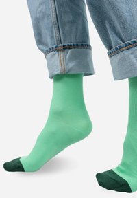 Zielone skarpetki z ciemniejszym zielonym palcem. Wykonane z gładkiego materiału, noszone z podwiniętą dżinsową spodnią, odsłaniając kostkę.