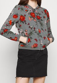 Szara kurtka z zamkiem błyskawicznym ozdobiona czerwonymi i różowymi kwiatami oraz zielonymi liśćmi. Długie rękawy, ściągacze przy mankietach i dwie boczne kieszenie. Czarna spódnica dżinsowa.