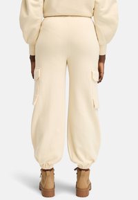 Crème cargo sweatpants met elastische boorden, zijzakken en een relaxed fit, gedragen met tan laarzen. Zachte textuur en casual ontwerp.