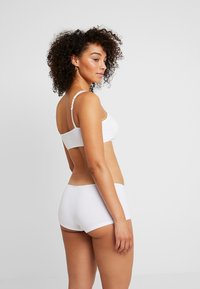 Weißes Baumwoll-Bralette- und Shorts-Set, das ein schlichtes Design, verstellbare Träger und klare Linien aufweist. Weiche, glatte Textur ohne Verzierungen.