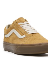 Baskets basses en daim beige avec bande blanche sur le côté, lacets blancs et semelle en caoutchouc marron, présentées en angle sur fond blanc.