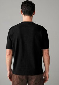 Black cotton t-shirt with short sleeves, crew neck design, smooth texture, and a relaxed fit. Back view shows minimalist styling without logos.