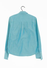Camicia azzurra a maniche lunghe, realizzata in tessuto morbido, presenta un retro con yoke, polsini con bottone e orlo arrotondato con spacchi laterali.