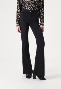 High-waisted black denim flared jeans with a textured finish, paired with a long-sleeve animal print top. Featuring a front button closure.