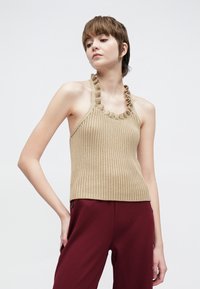 Beige geribd haltertop met een geruffelde halslijn. Getailleerd ontwerp met een gladde textuur, gecombineerd met bordeauxrode broek.