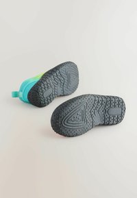 Due scarpe da ginnastica con suola in gomma nera caratterizzata da modelli di presa testurizzati. La parte superiore presenta un gradiente di materiali in acquamarina e verde chiaro.