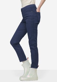 Námořnické modré úzké džíny s bočním lemováním, vyrobené z bavlněné směsi. V kombinaci s duhovými gumovými botami a svetrem světlé barvy.