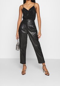 Svart paljettcamisole med tunna band, kombinerad med högmidjade svarta läderbyxor och svarta sandaler med klack.