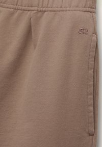 Pantaloni della tuta color taupe realizzati in morbido cotone, con vita elastica e tasca laterale. Logo tono su tono ricamato sulla gamba.