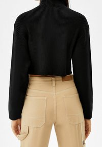 Svart ribbad polotröja i cropped-längd; matchas med beiga cargobyxor med dubbla bakfickor och kontrasterande sömmar.