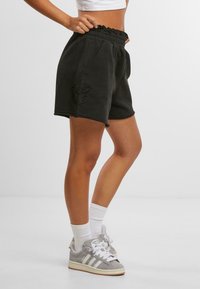 Sorte bomullsshorts med elastisk volangliv, to sidelommer, en sommerfugl broderi detaljer på venstre side, og en frayed kant.