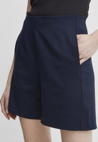 Navyblå shorts lavet af blødt stof med en tætsiddende talje, der har forlommer og rene linjer for et skræddersyet udseende.