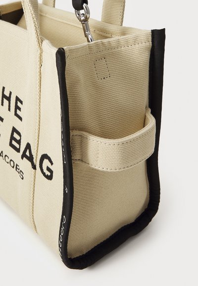 Canvas tote bag i ljusbeige med svarta detaljer. Har en sidoficka, djärv textdesign och ett robust handtag. Strukturerad tygfinish.