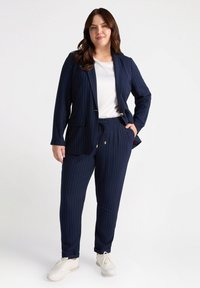 Marinblå rutig kostym med skräddarsydd blazer och byxor med elastisk midja. Vit T-shirt under. Modellen bär vita sneakers.