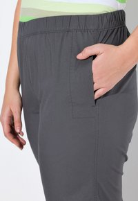 Grijze elastische taillebandbroeken met een zijzak, voorzien van een gladde textuur en een rechte pijpdesign. Close-upweergave benadrukt de stofdetails.