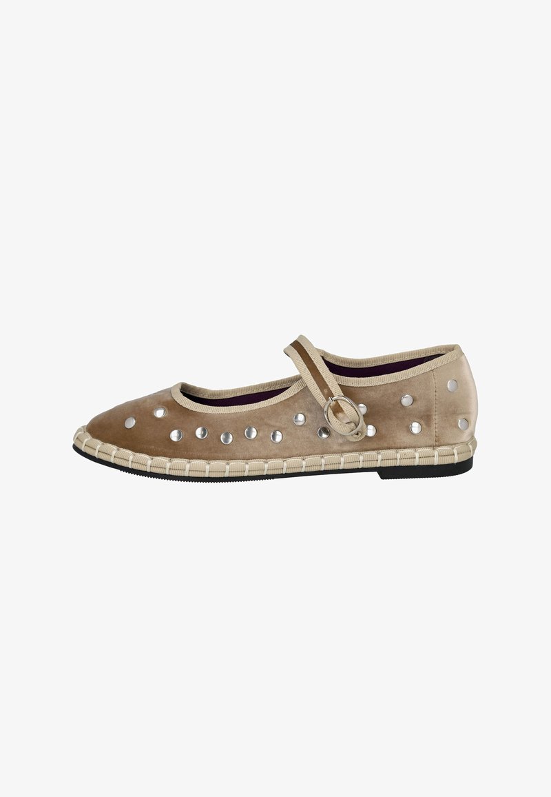 Zapato de ante beige con puntera redonda, tachuelas decorativas plateadas y una correa. Presenta un borde delimitado y una suela de goma negra. Diseño ligero.