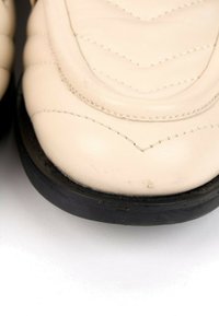 Gros plan sur la pointe d'une chaussure en cuir blanc avec des coutures détaillées et une semelle noire sur fond blanc.