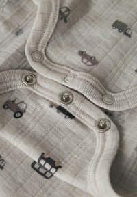 Tessuto beige chiaro con piccoli motivi di camion e orsi scuri, caratterizzato da bottoni a pressione argentati lungo il bordo e materiale morbido e testurizzato.