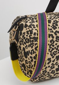 Borsa a viaggio in stampa leopardata con accessori neri e dorati, e una tracolla gialla con strisce verdi e viola.