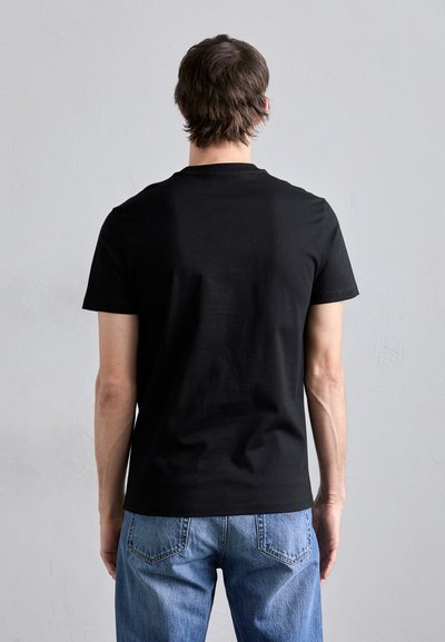 T-shirt noir à manches courtes en coton doux, avec un col rond. Porté avec un jean en denim bleu légèrement délavé, offrant une coupe décontractée.