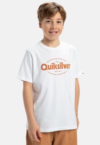 Bílá bavlněná tričko s kulatým výstřihem, s oranžovým logem "Quiksilver" a textem. Krátké rukávy, uvolněný střih, s viditelnými švy.