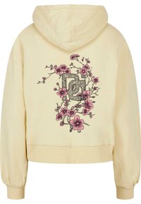 Haut à capuche crème avec cordon de serrage, poignets côtelés et un design complexe de fleurs roses autour d'un logo central.