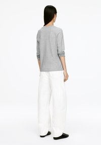 Gray long-sleeve shirt paired with white wide-leg trousers and black shoes. The shirt has rolled sleeves and a rounded neckline.