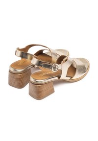 Sandali con tacco metallici dorati, design con strappi incrociati e dettaglio con fibbia circolare. Tacco a blocco in legno texturizzato e plantare liscio.