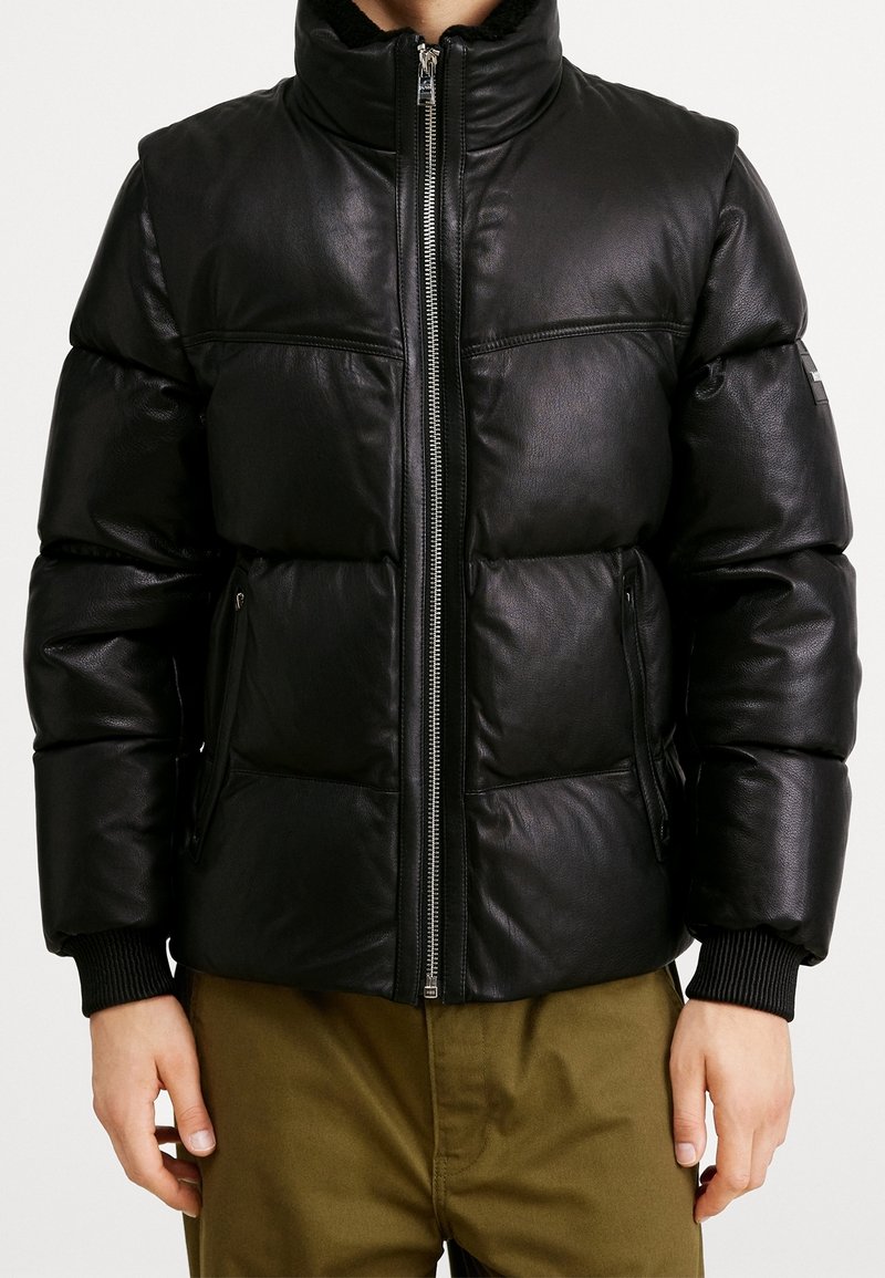 Svart läderpuffjacka med hög krage, dragkedja fram, ribbade ärmmuddar och sidofickor; har en slät textur och quiltat mönster.