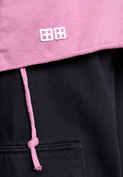 Prenda de algodón rosa con una cinturilla negra, que presenta un logo blanco en la parte frontal y un detalle de cordón rosa en la cinturilla.