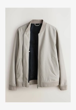Svetlosivá bomber bunda s textúrovaným vonkajším povrchom, rebrovanými manžetami a čiernym vnútrom. Má bočné vrecká a predné zapínanie na zips.