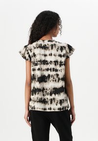 Svart og kremfarget tie-dye topp med korte ermer, volanger på ermene og løs passform, med buet hem og myk, lett tekstur.